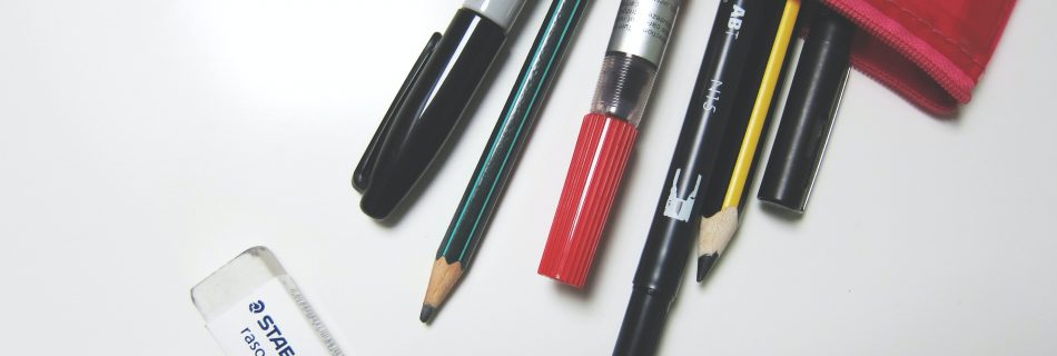 Picture shows a part of a red and black pencil case lying on a white surface with the zip open and pens and pencils spilling out. A white eraser lies next to them.